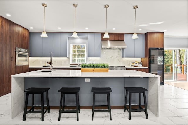 kitchen with a large island, wall chimney range hood, stainless steel appliances, and hanging light fixtures