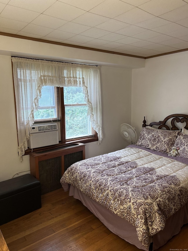 bedroom with cooling unit, wood finished floors, crown molding, and radiator heating unit