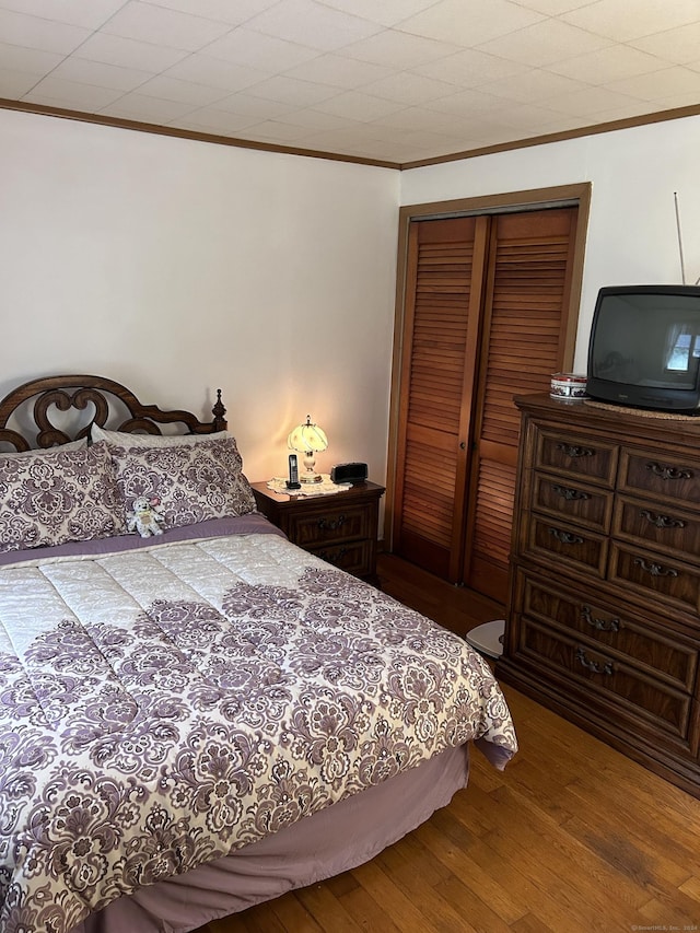 bedroom with crown molding, wood finished floors, and a closet