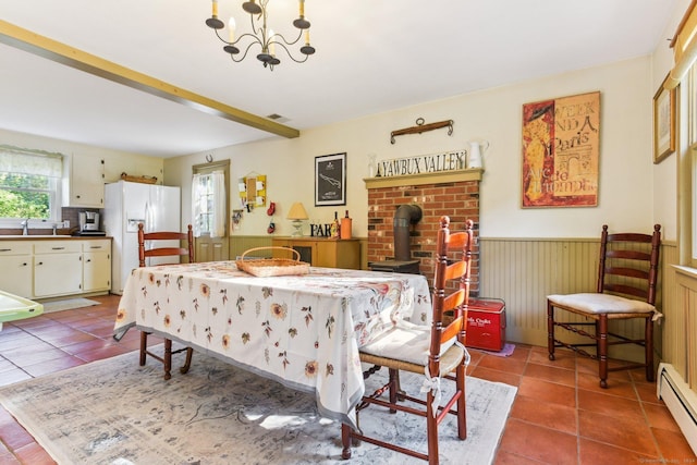 tiled dining space featuring an inviting chandelier, a baseboard heating unit, sink, and a wood stove