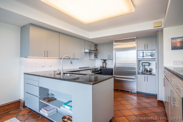 kitchen featuring dark tile patterned flooring, kitchen peninsula, built in appliances, dark stone counters, and sink