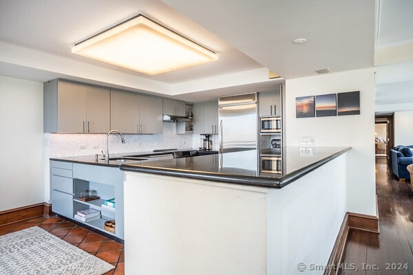 kitchen featuring dark wood-type flooring, kitchen peninsula, built in appliances, and sink