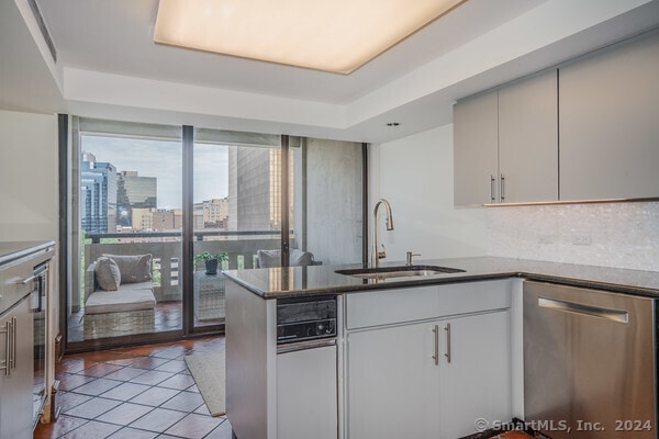 kitchen with sink, kitchen peninsula, dishwasher, a tray ceiling, and light wood-type flooring