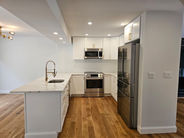 kitchen with light stone countertops, sink, stainless steel appliances, kitchen peninsula, and white cabinets