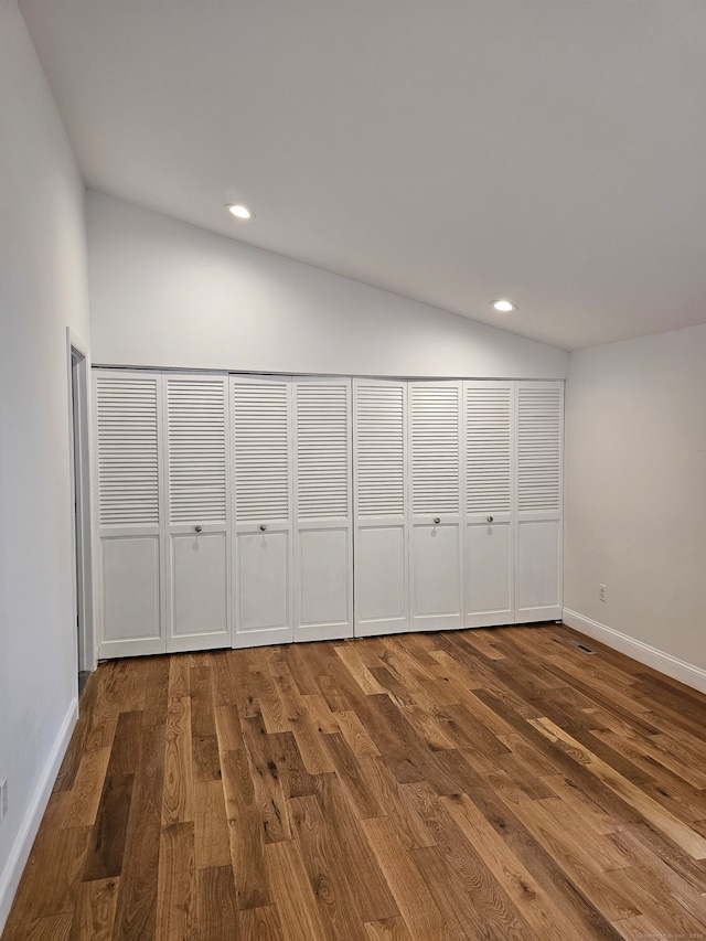 unfurnished bedroom with wood-type flooring, lofted ceiling, and two closets