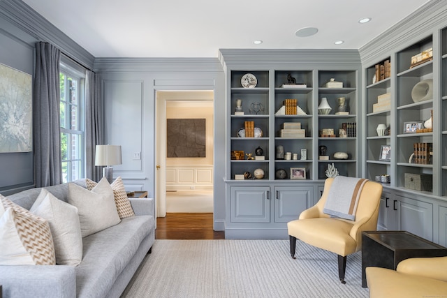 living area with built in features, hardwood / wood-style floors, and ornamental molding