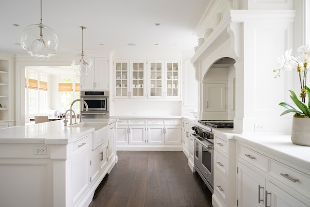 kitchen featuring range with two ovens, a kitchen island with sink, dark wood-type flooring, sink, and white cabinetry