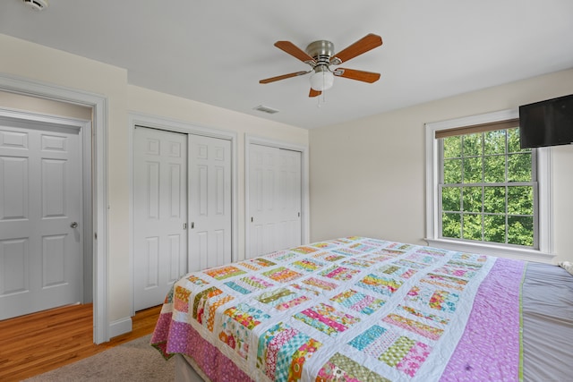 bedroom with ceiling fan, wood-type flooring, and multiple closets