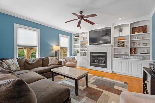 living room featuring built in features, ceiling fan, light hardwood / wood-style floors, and crown molding