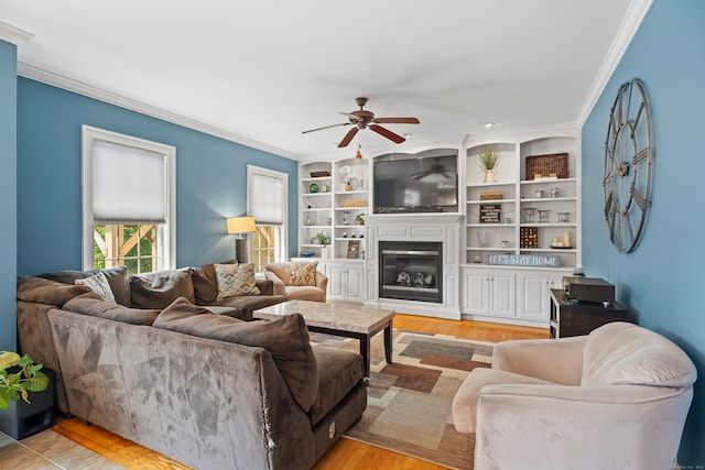 living room with built in features, crown molding, ceiling fan, and light hardwood / wood-style floors