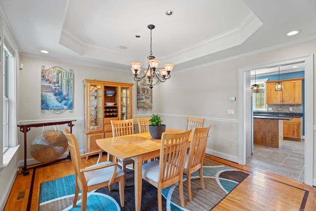 dining area featuring crown molding, a notable chandelier, light hardwood / wood-style flooring, and a raised ceiling