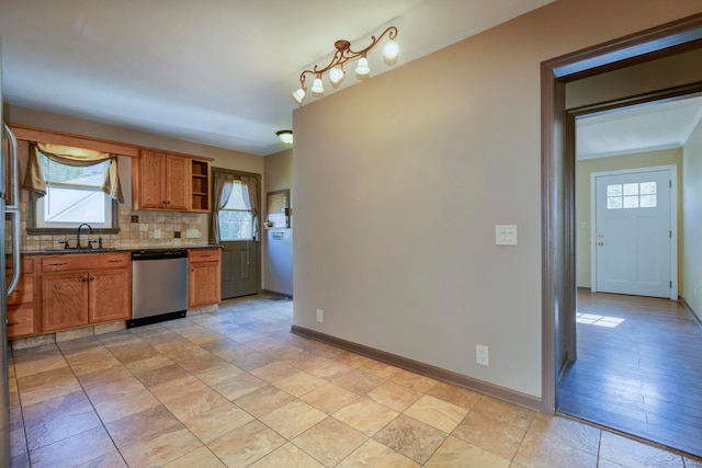 kitchen featuring dark stone counters, backsplash, sink, stainless steel dishwasher, and light hardwood / wood-style flooring