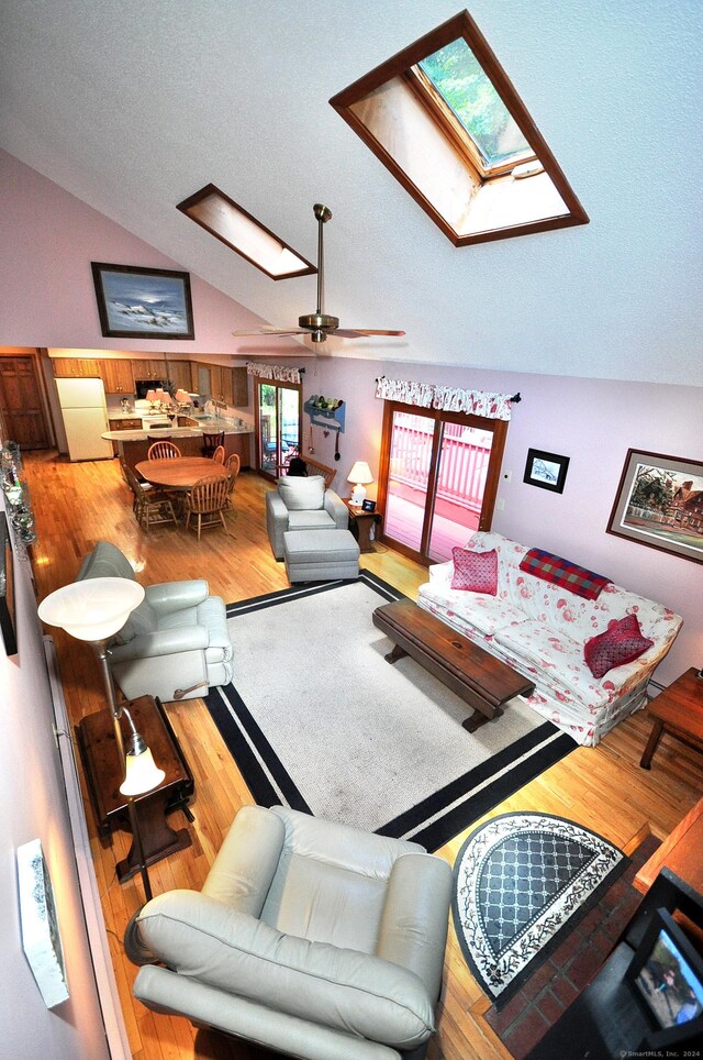 living room featuring lofted ceiling with skylight, hardwood / wood-style floors, ceiling fan, and a textured ceiling