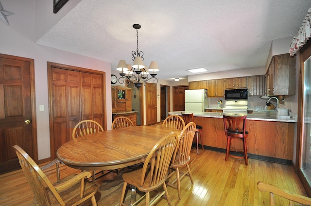 dining area with a notable chandelier, sink, light wood-type flooring, and a textured ceiling