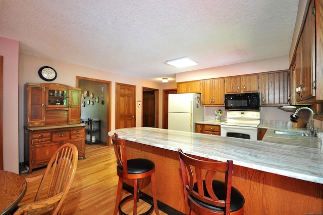 kitchen featuring kitchen peninsula, a textured ceiling, white appliances, sink, and light hardwood / wood-style floors