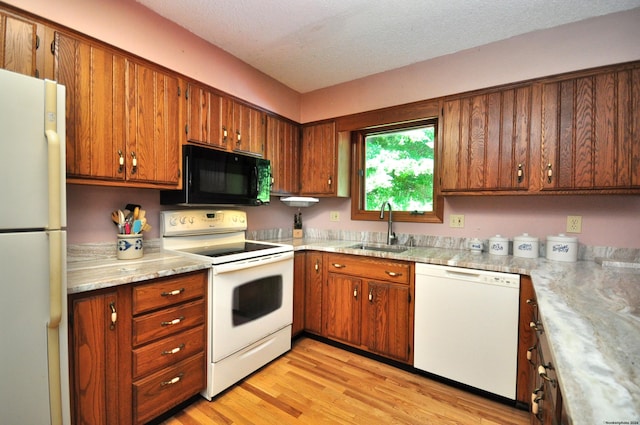 kitchen with a textured ceiling, light wood-type flooring, white appliances, and sink