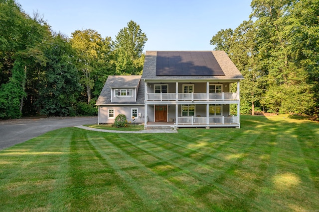 view of front facade featuring a balcony, solar panels, a front lawn, and a porch