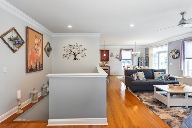 living room featuring ornamental molding, light wood-type flooring, and ceiling fan with notable chandelier