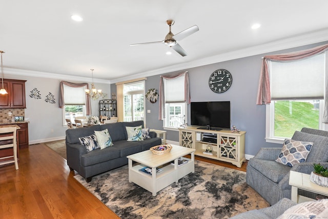 living room with ceiling fan with notable chandelier, crown molding, dark wood-type flooring, and a wealth of natural light