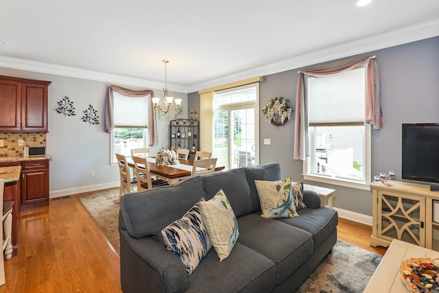 living room with light wood-type flooring, crown molding, a chandelier, and a wealth of natural light