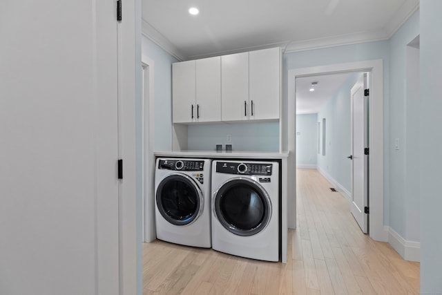 laundry room with light wood-type flooring, washer and clothes dryer, ornamental molding, and cabinets