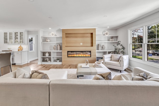 living room with crown molding, a large fireplace, and light hardwood / wood-style flooring