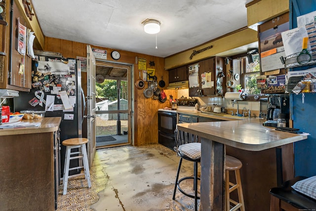 kitchen featuring wooden walls, black range with electric cooktop, a kitchen bar, and kitchen peninsula