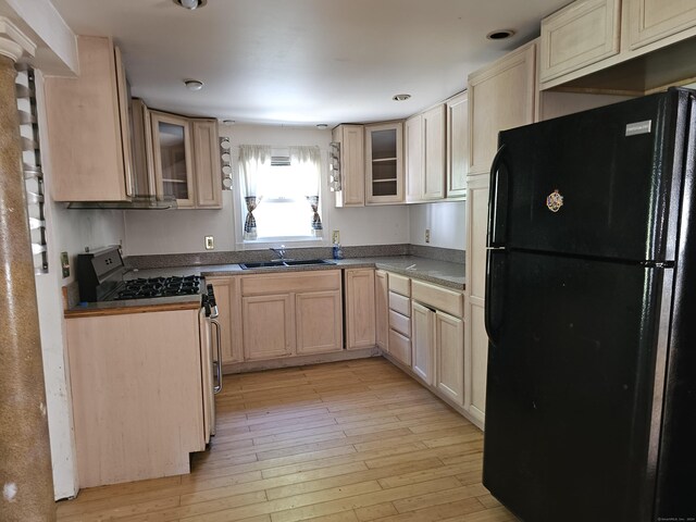 kitchen featuring black refrigerator, gas stove, sink, light brown cabinets, and light hardwood / wood-style floors