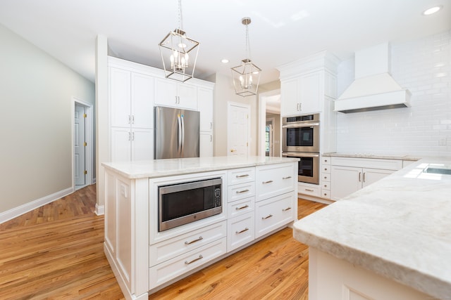 kitchen featuring premium range hood, white cabinetry, stainless steel appliances, hanging light fixtures, and a center island