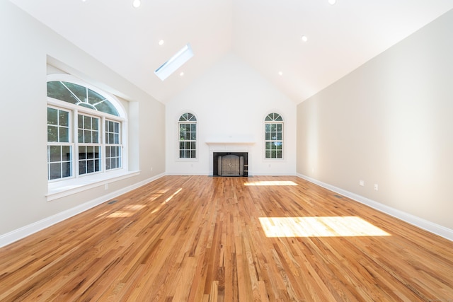 unfurnished living room featuring high vaulted ceiling, light hardwood / wood-style flooring, and a skylight