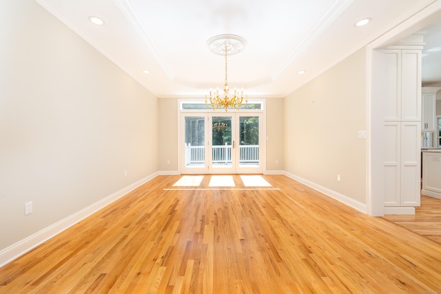 unfurnished dining area featuring a notable chandelier, a tray ceiling, light wood-type flooring, ornamental molding, and french doors