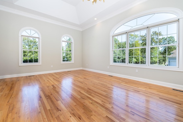 empty room featuring crown molding, a tray ceiling, a chandelier, and light hardwood / wood-style flooring