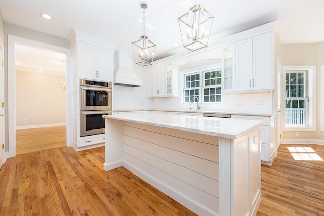 kitchen featuring stainless steel double oven, premium range hood, white cabinetry, and a center island