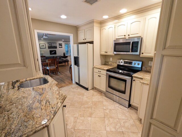 kitchen featuring light stone counters, recessed lighting, a sink, stainless steel appliances, and cream cabinets