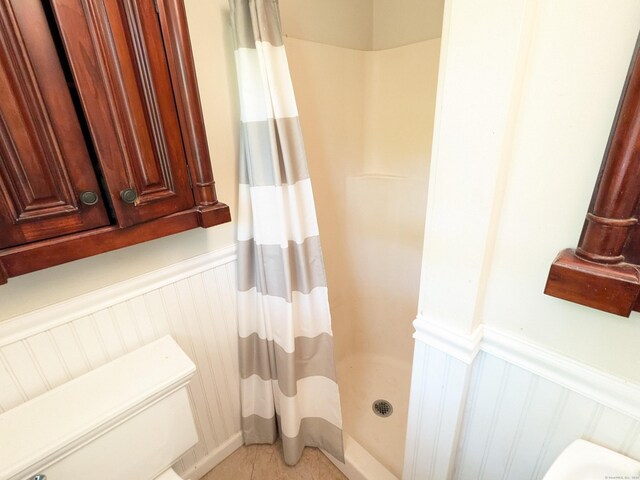 bathroom with tile patterned floors, a wainscoted wall, and a shower stall