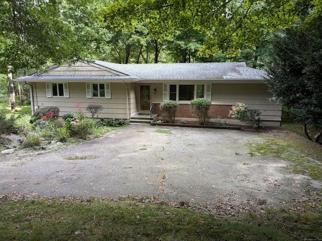 ranch-style home with aphalt driveway, brick siding, and roof with shingles