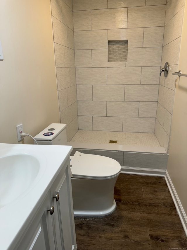 bathroom featuring tiled shower, toilet, vanity, and hardwood / wood-style flooring