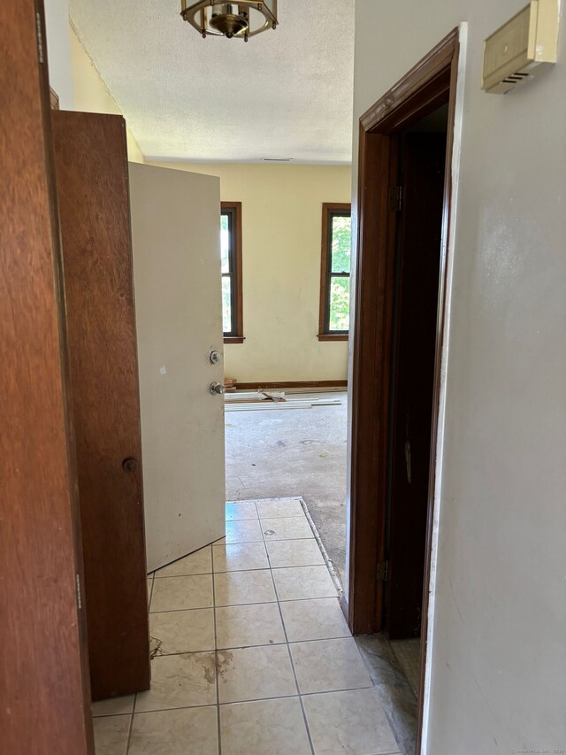 hallway with a textured ceiling and light tile patterned floors