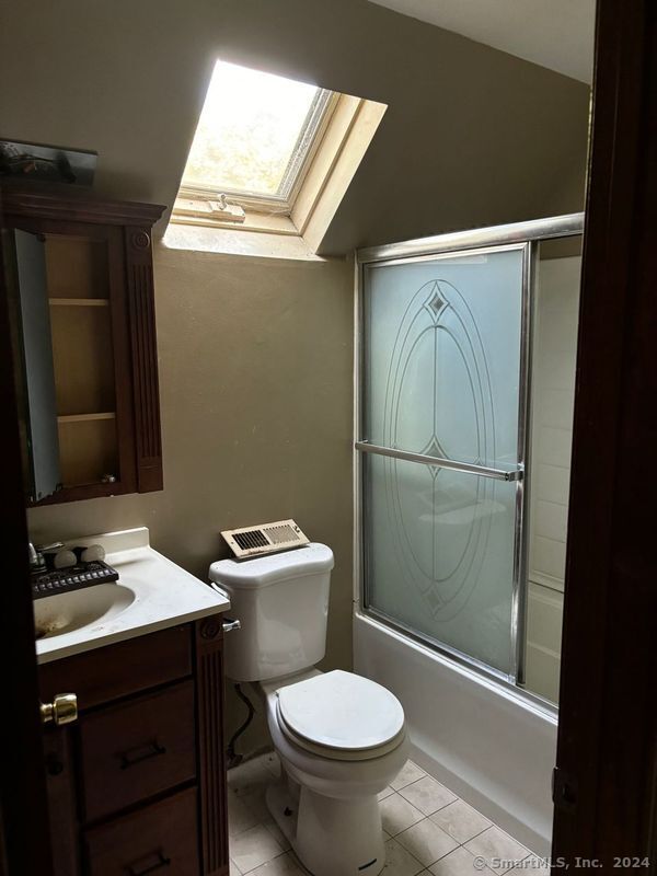 full bathroom featuring vanity, a skylight, combined bath / shower with glass door, tile patterned floors, and toilet