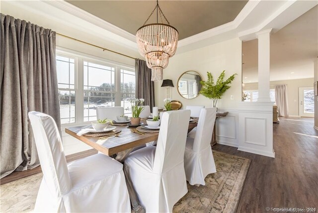 dining space with dark wood-type flooring, a raised ceiling, a notable chandelier, and ornate columns