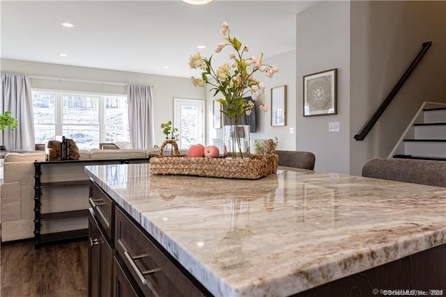 kitchen featuring light stone countertops, dark brown cabinetry, open floor plan, recessed lighting, and dark wood-style flooring