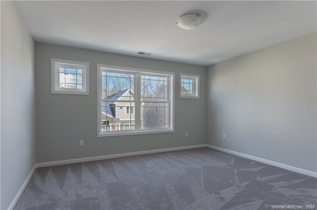 carpeted empty room featuring a healthy amount of sunlight, visible vents, and baseboards