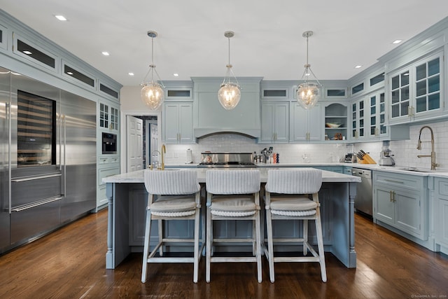 kitchen featuring tasteful backsplash, stainless steel appliances, a kitchen island with sink, sink, and pendant lighting