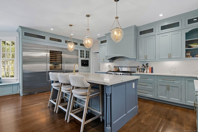 kitchen with appliances with stainless steel finishes, dark hardwood / wood-style floors, a kitchen island with sink, and pendant lighting