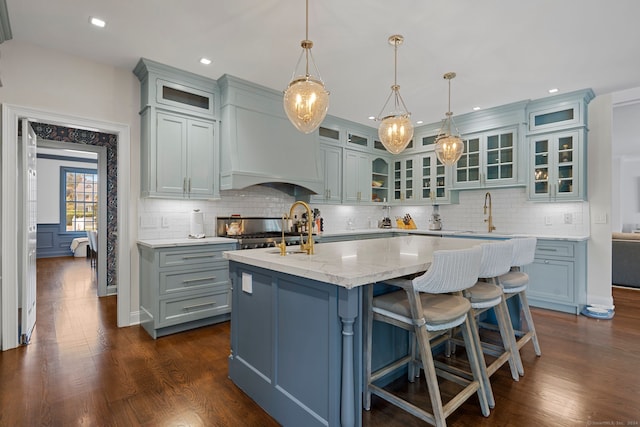 kitchen with tasteful backsplash, a kitchen island with sink, dark wood-type flooring, sink, and pendant lighting