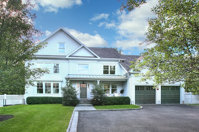 view of front of home with a front lawn, a standing seam roof, aphalt driveway, fence, and covered porch