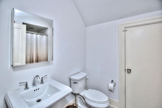 full bathroom with a sink, baseboards, toilet, and vaulted ceiling