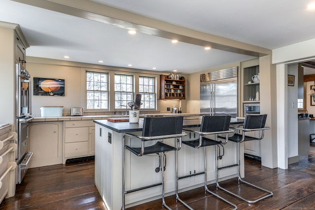 kitchen featuring built in fridge, dark hardwood / wood-style flooring, a center island, and a kitchen breakfast bar