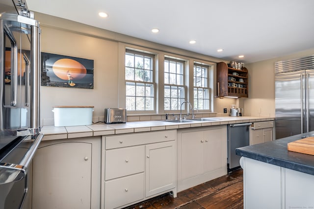 kitchen with dark hardwood / wood-style floors, stainless steel built in fridge, tile countertops, sink, and white cabinetry