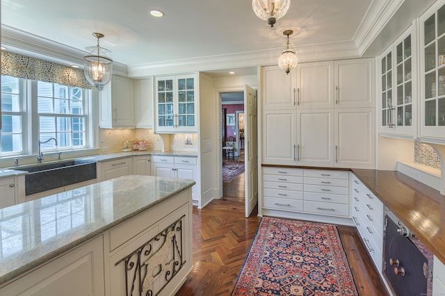 kitchen featuring hanging light fixtures, white cabinets, a sink, ornamental molding, and light stone countertops